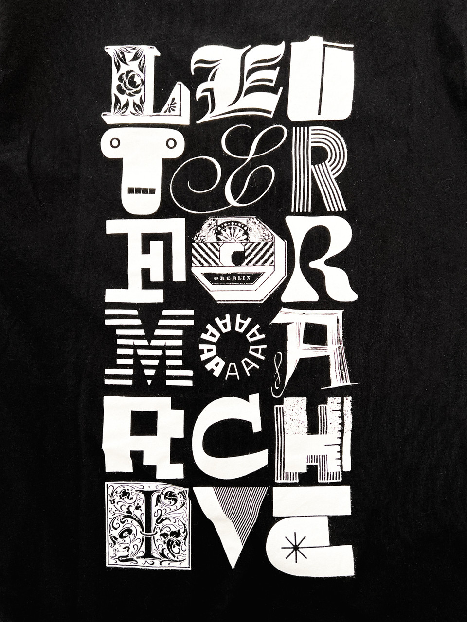 Photo of black t-shirt back with the words “LETTERFORM ARCHIVE” in three columns of letters from various sources.