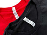 Photo of tags from red and black t-shirts showing Canvas brand and 100% cotton.